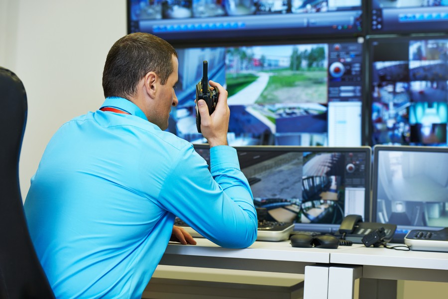 Security guard monitoring surveillance footage and relaying information via a walkie-talkie. 