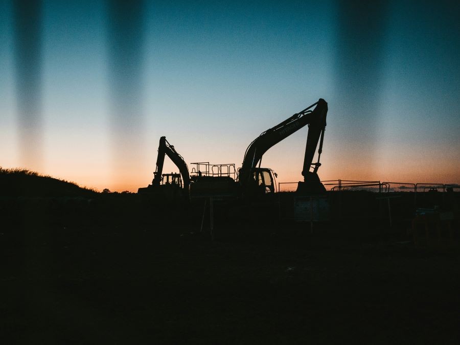 An excavator behind a fence at sunset.