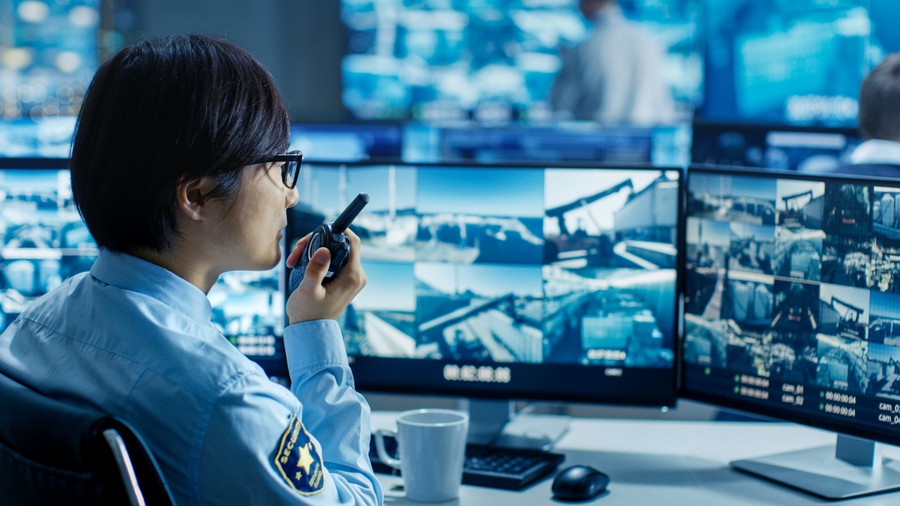 Security operator monitoring multiple surveillance camera feeds in a remote security monitoring center.
