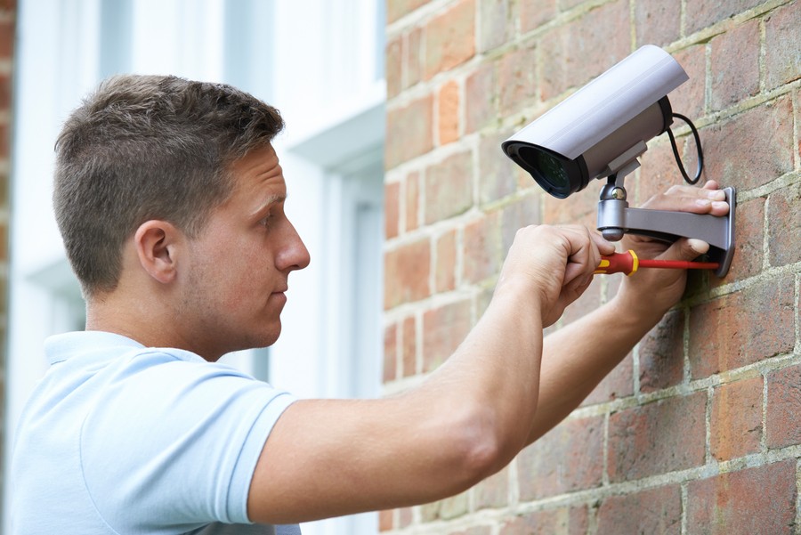 a man installing a security camera on a bricked wall 