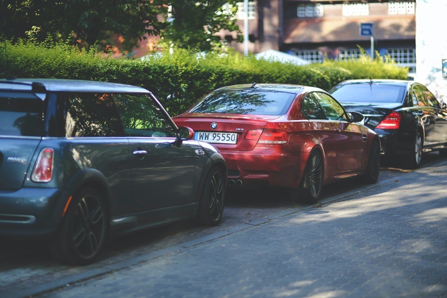 Three cars parked along the curb, green hedges in the background. 