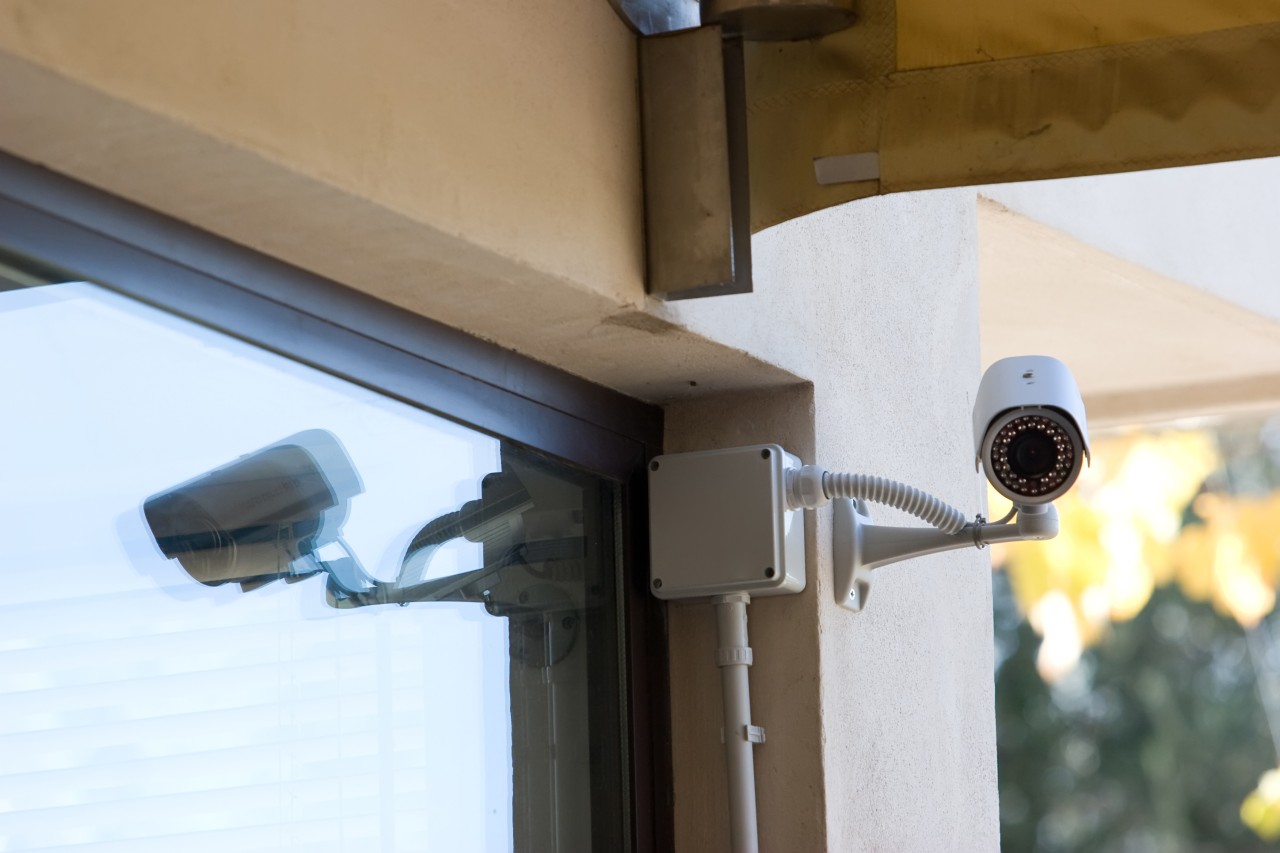 Photo of a security camera mounted on the front glass door of a business.